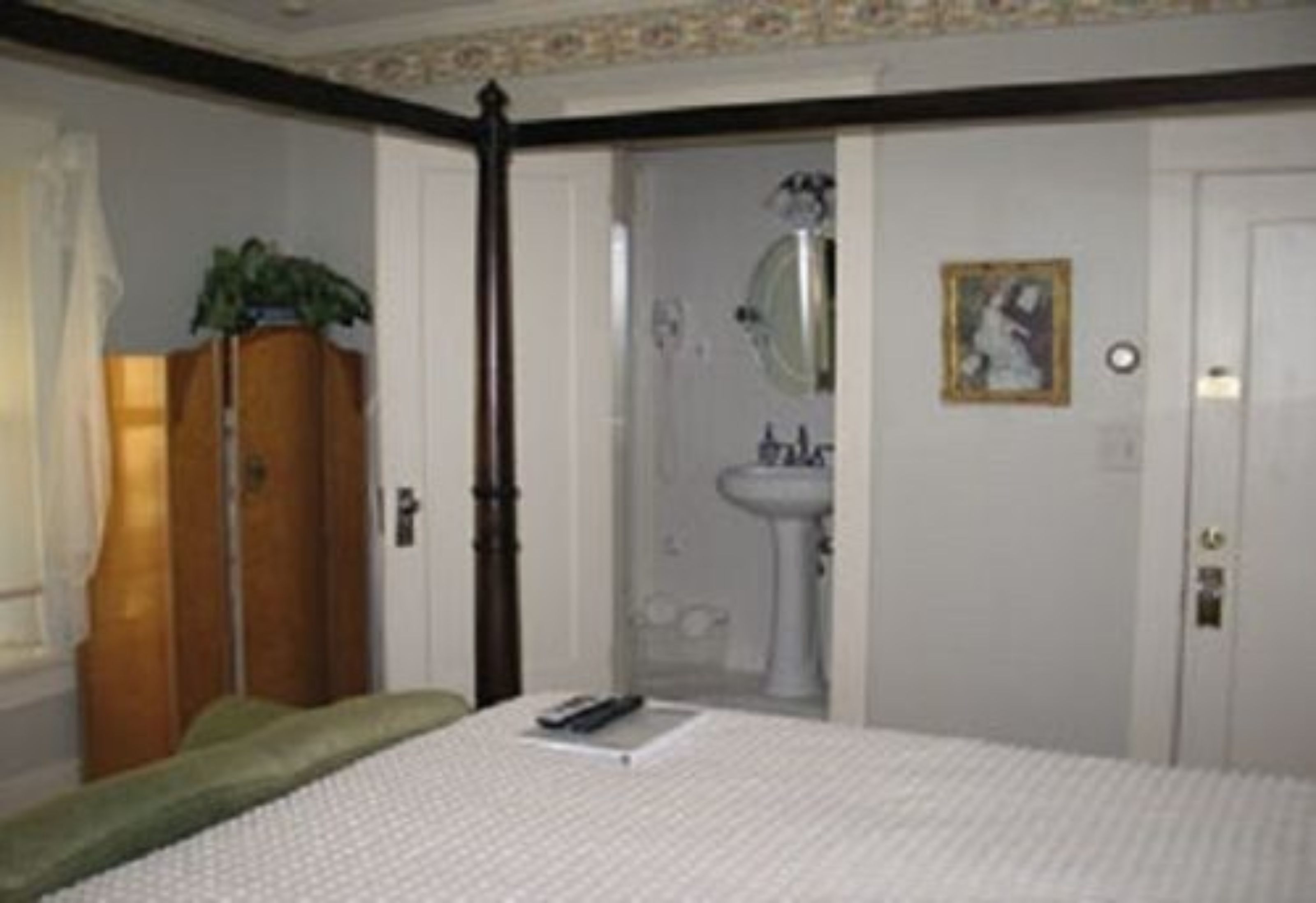Quarto com cama, mesa de cabeceira, guarda-roupa, espelho e banheiro visível por uma porta aberta.