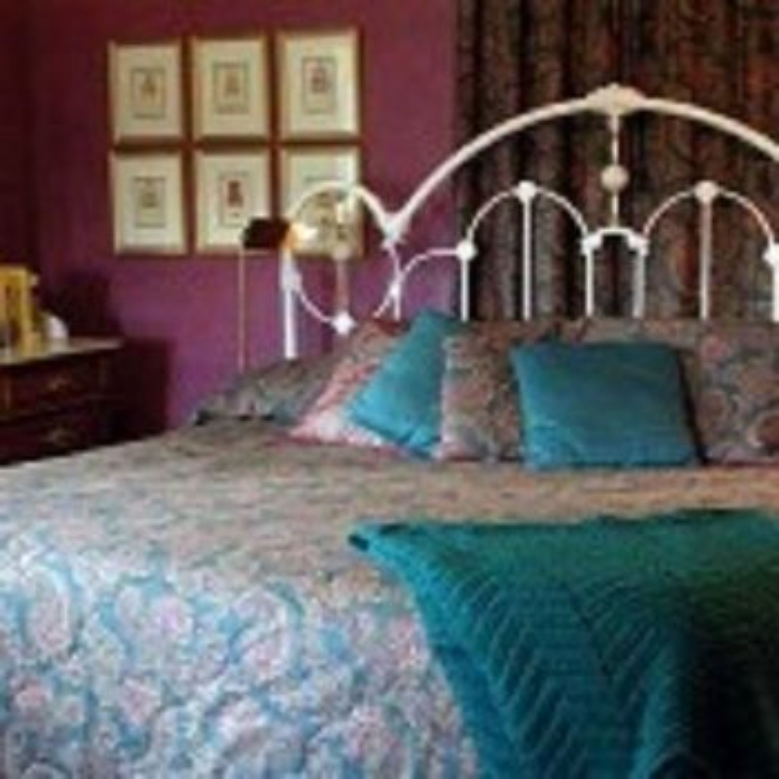A bedroom with a four-poster bed, a bedside table, and a wall with framed pictures.