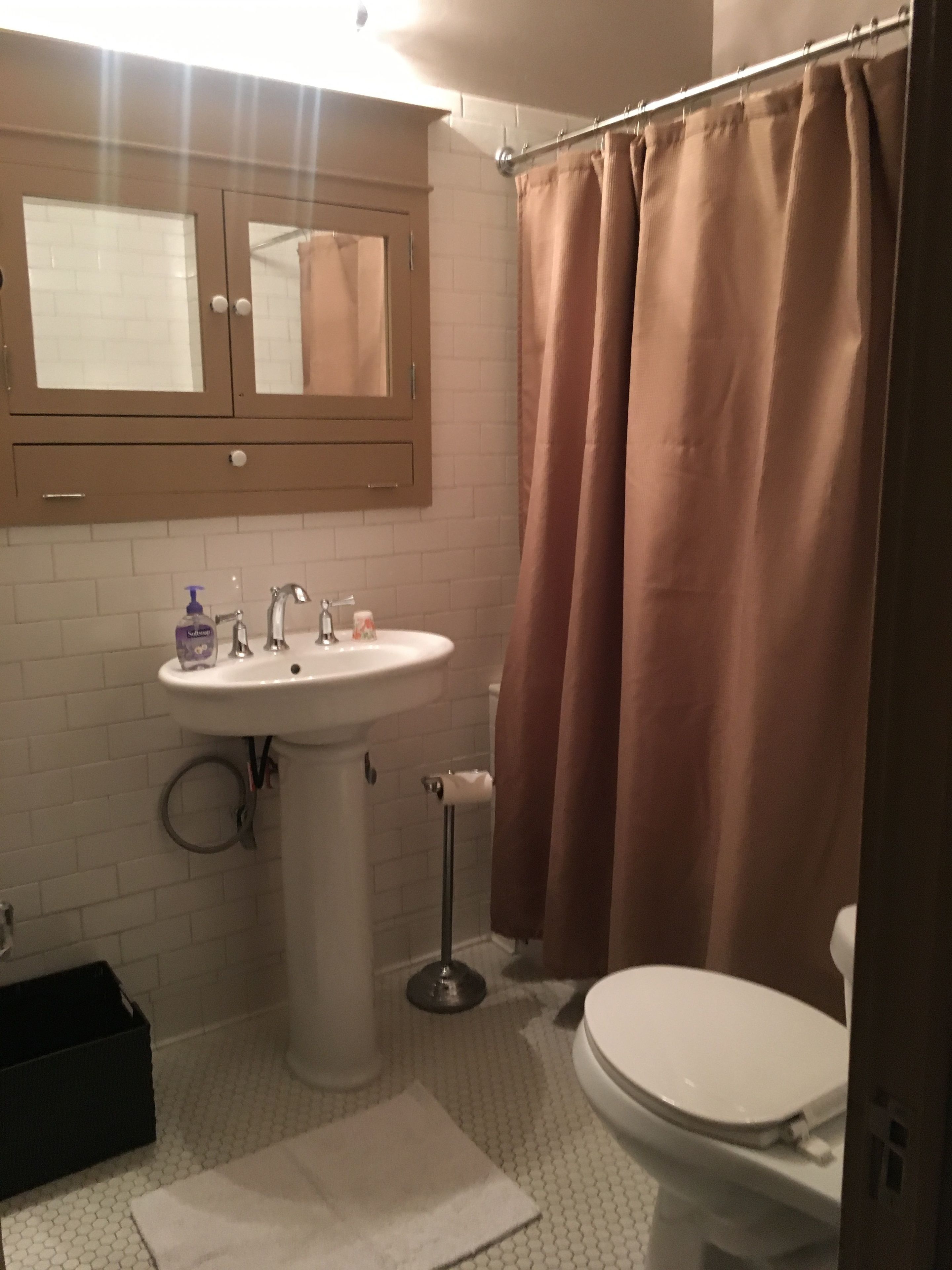 Ein Badezimmer mit weißem Waschbecken, einem Spiegel, einer Toilette und einer Duschvorhang.
