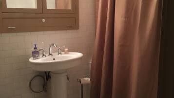 Ein Badezimmer mit weißem Waschbecken, einem Spiegel, einer Toilette und einer Duschvorhang.