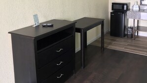 Habitación de hotel con una televisión de pantalla plana montada en la pared, un escritorio pequeño con cajones, un microondas y un cubo de basura.