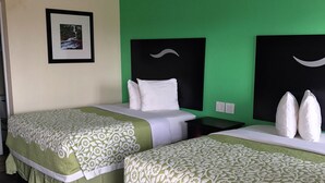 Habitación de hotel con dos camas, cada una con ropa de cama blanca y verde con motivos florales, un cuadro en la pared y una pared de acento verde.