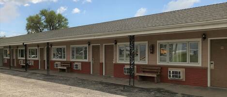 A motel with a row of rooms, each with a window and a bench outside.