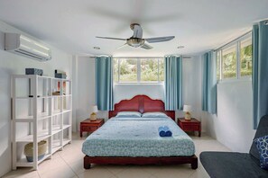Un dormitorio con cama, ventilador de techo, armario y ventana con cortinas.