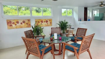 A dining area with a round table, six wooden chairs with blue cushions, and two ceiling fans.