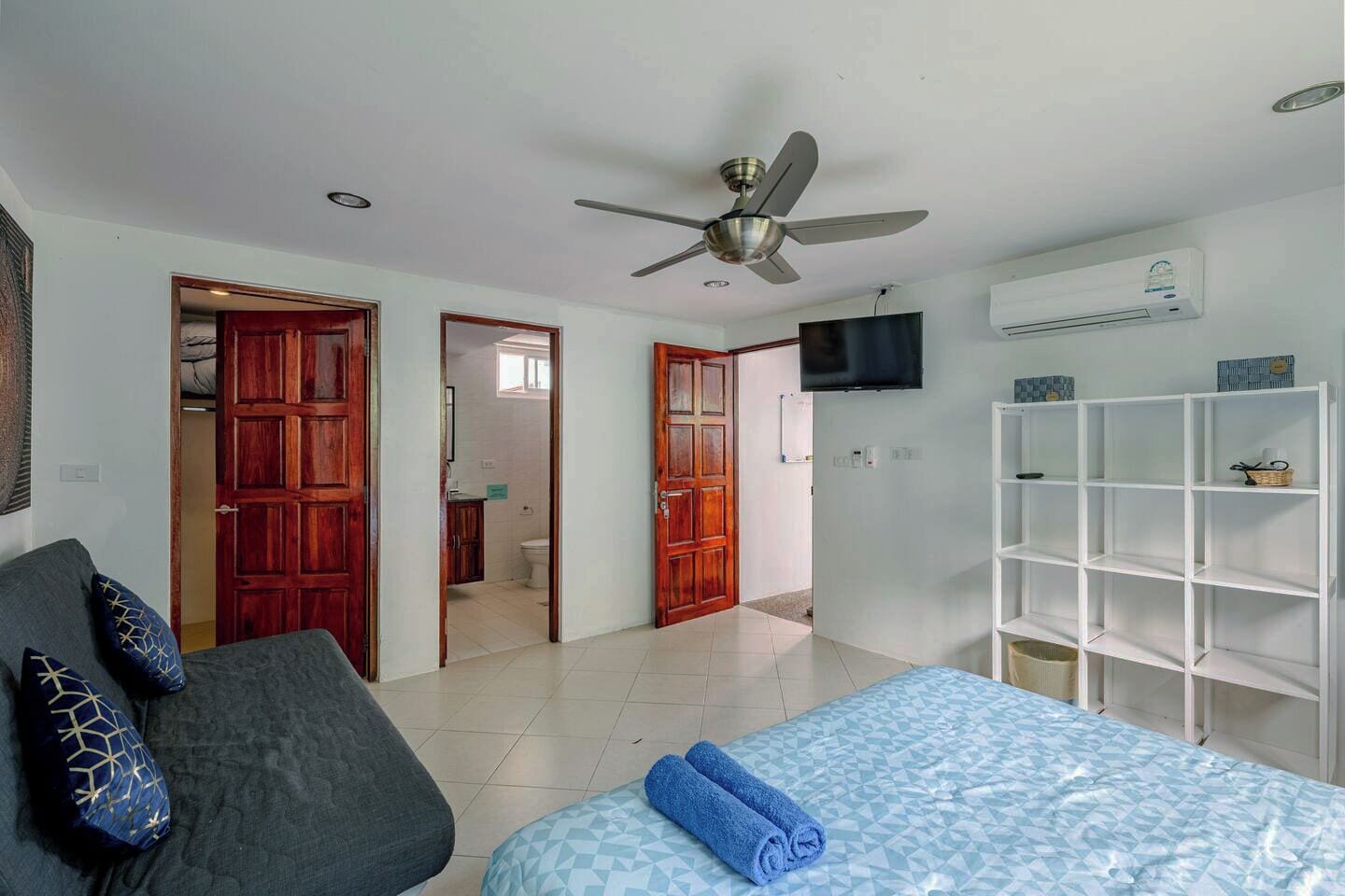 Ein Schlafzimmer mit einem Bett, einem Deckenventilator, einem Fernseher und einem weißen Regal.