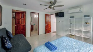 A bedroom with a bed, a ceiling fan, a TV, and a white shelving unit. - Kamala Heights (Kamala)