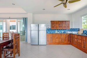 A modern kitchen with wooden cabinets, a stainless steel refrigerator, and a dining area with a table and chairs. - Kamala Heights (Kamala)