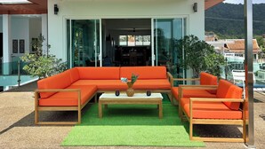 A modern outdoor seating area with a glass enclosure, a wooden coffee table, and orange furniture. - Kamala Heights (Kamala)