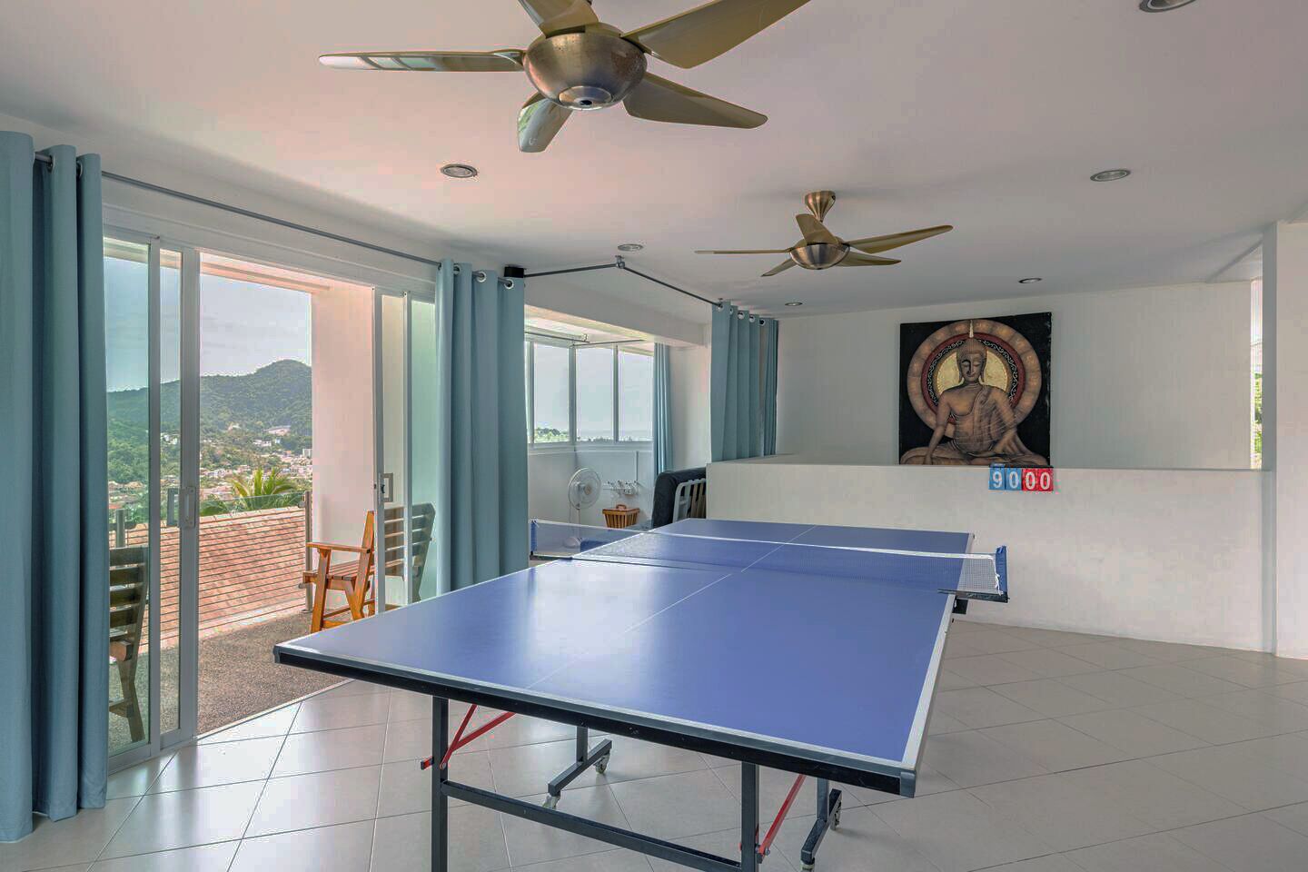 A spacious room with a ping pong table, ceiling fans, large windows, and a mural on the wall.