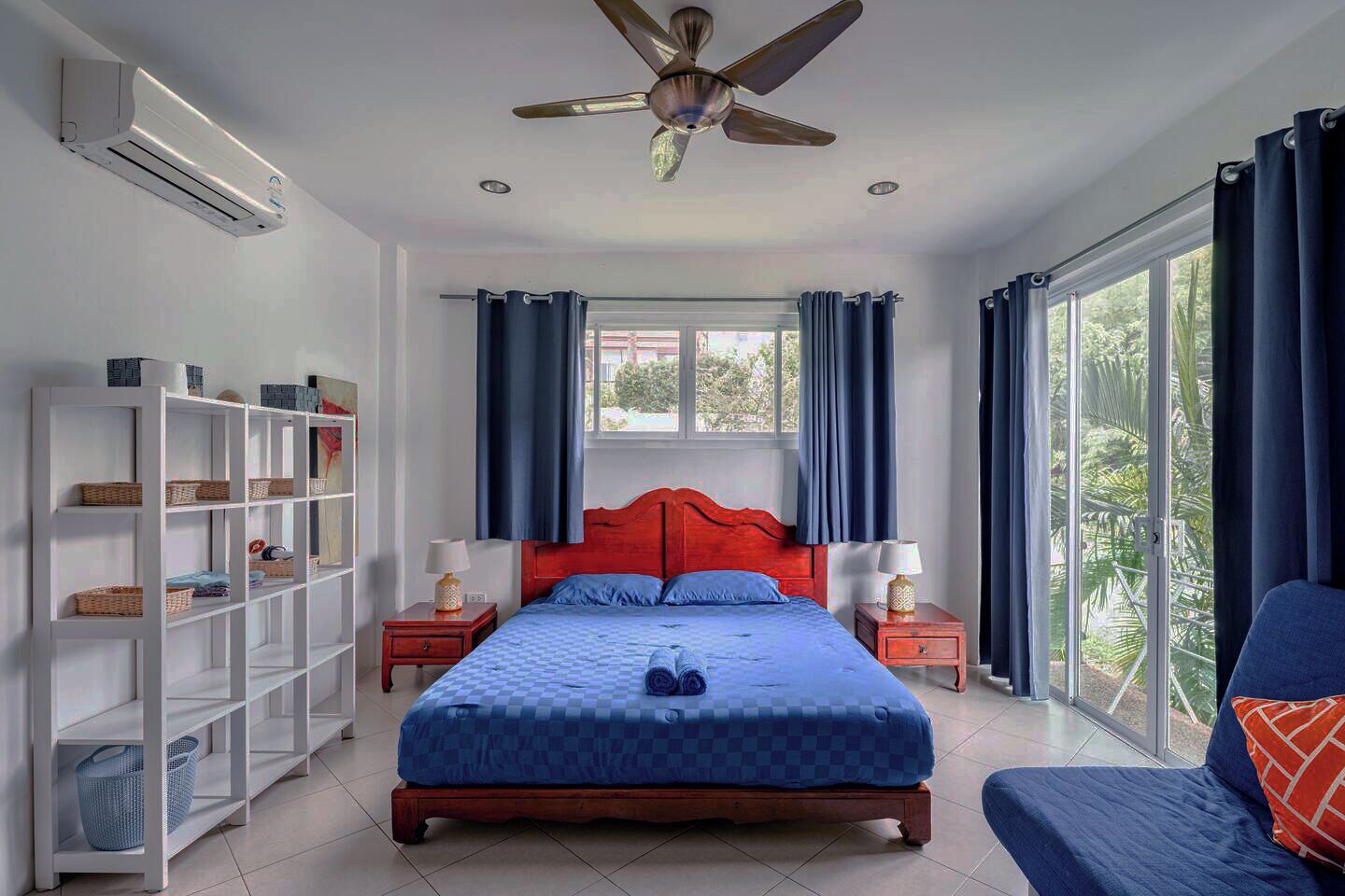 A bedroom with a bed, a ceiling fan, a window with curtains, a bookshelf, and a nightstand.