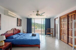 A bedroom with a bed, a ceiling fan, a nightstand, a chair, and a view of the outdoors. - Kamala Heights (Kamala)