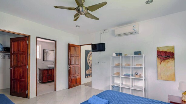 Habitació d'hotel amb dos llits, un ventilador de sostre, una televisió, una estanteria i un quadre.