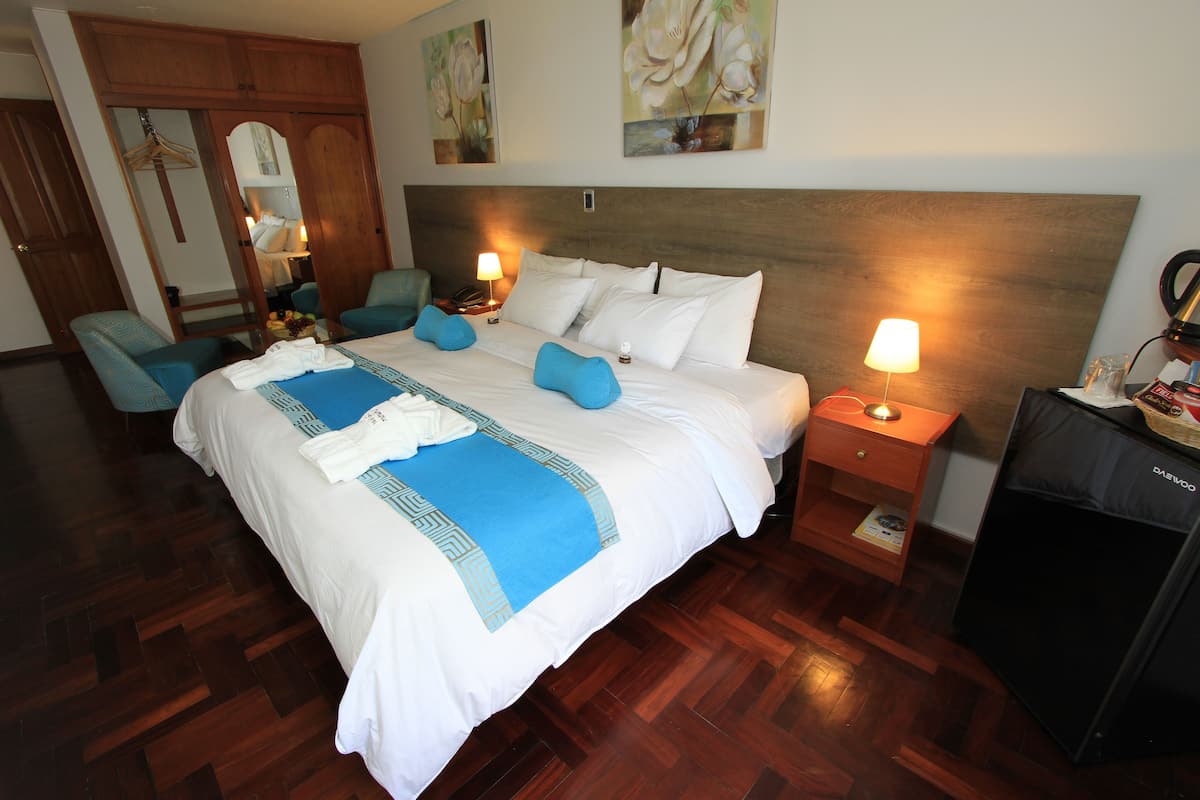 Una habitación de hotel con una cama grande, dos mesitas de noche con lámparas, un armario de madera y un escritorio con lámpara.