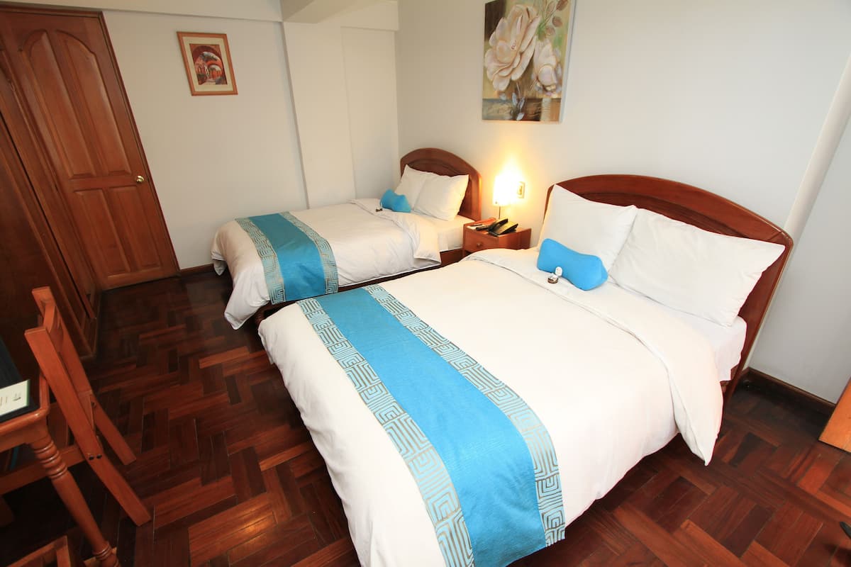Habitación de hotel con dos camas, suelo de madera, un armario de madera y una mesita de noche con lámpara.