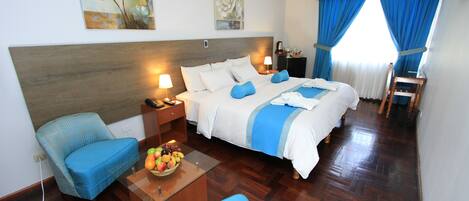 Habitación de hotel con cama, dos sillas, una mesita de noche, lámpara y obras de arte en las paredes.