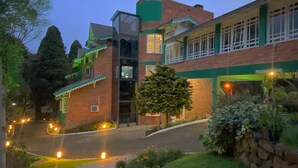 A two-story building with a green and white facade, a glass elevator, and a stone wall with plants. - Hotel Pousada Ald'Mama (Gramado)