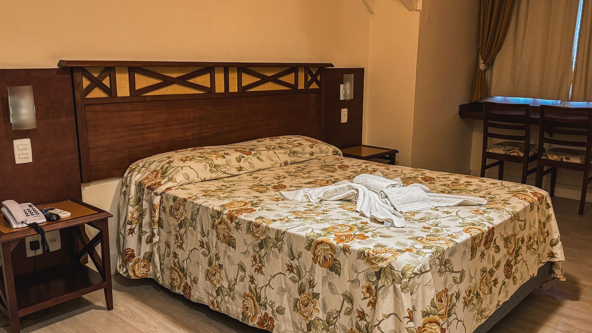 Una habitación de hotel con una cama, un escritorio y una silla. Hay un teléfono en la mesita de noche.