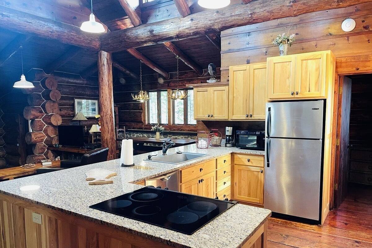 A rustic kitchen with wooden cabinets, a stainless steel refrigerator, and a granite countertop.