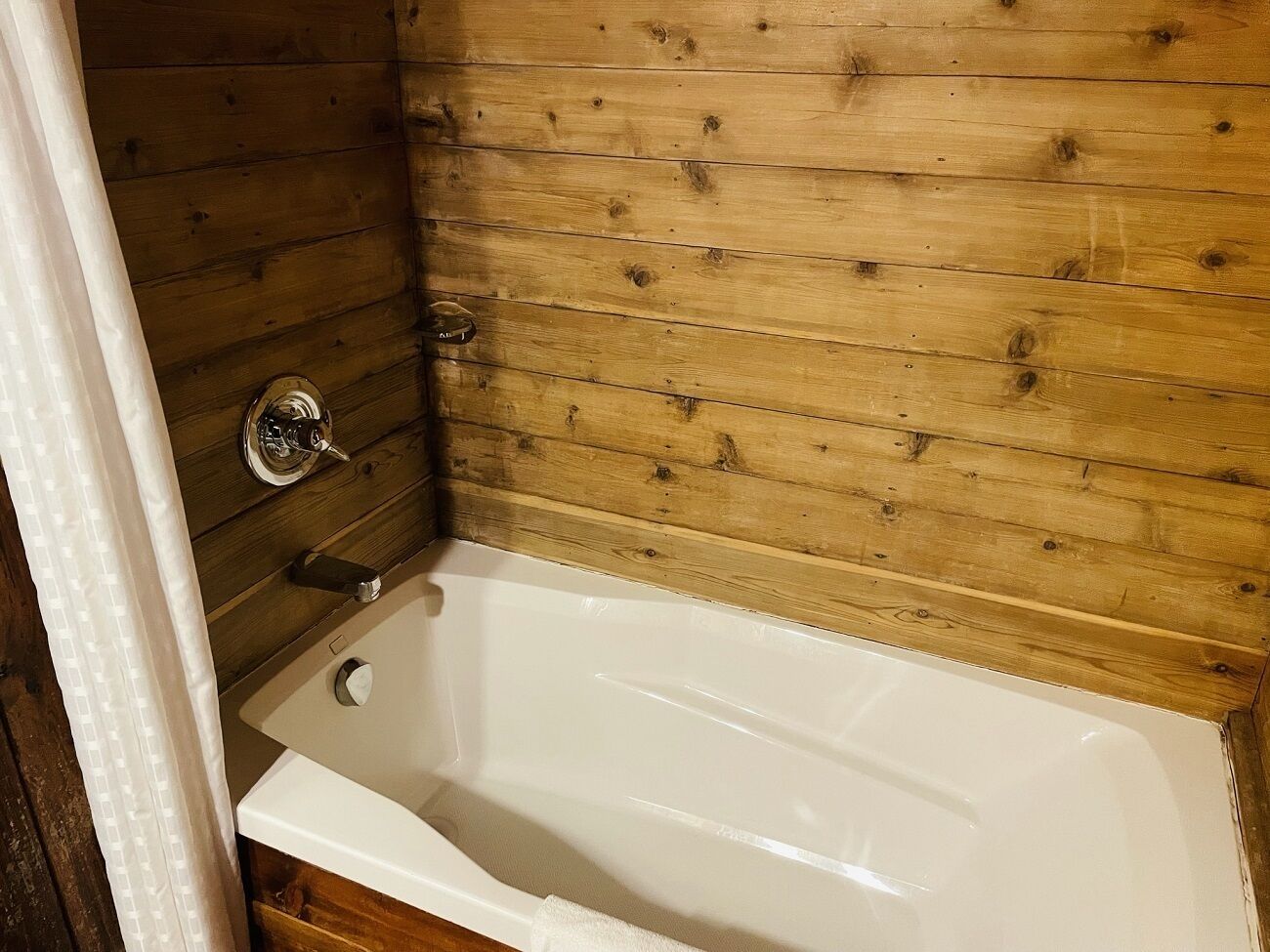 A bathroom with a wooden wall, a white bathtub, and a chrome faucet.