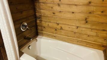 A bathroom with a wooden wall, a white bathtub, and a chrome faucet.