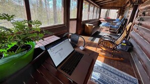 A cozy cabin interior with a laptop on a wooden desk, a rocking chair, and a large window overlooking trees. - Drummond Island Resort (Drummond Island)