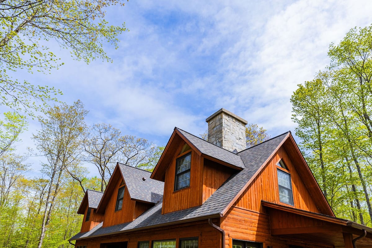 A wooden cabin with a deck, large windows, and a chimney.