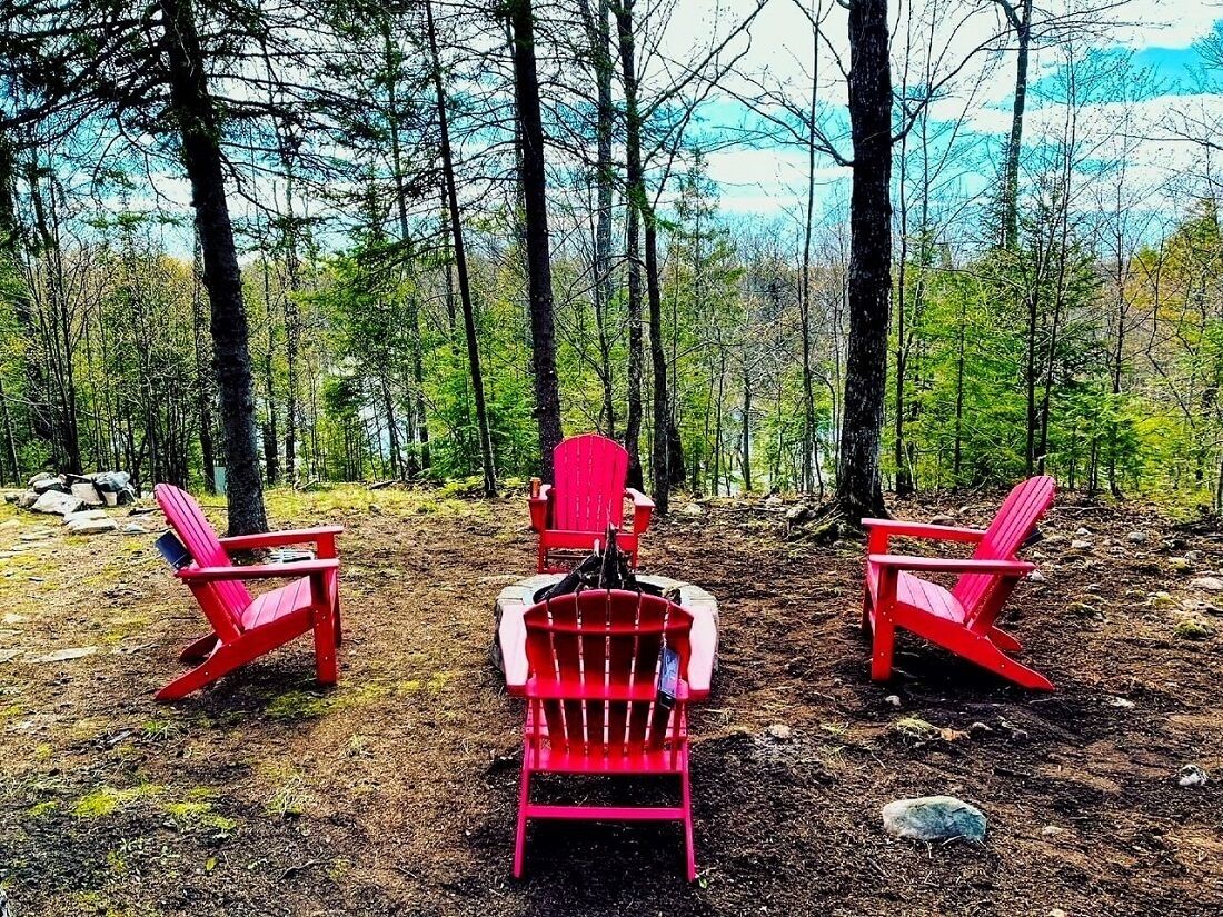Three red Adirondack chairs in a forest setting.