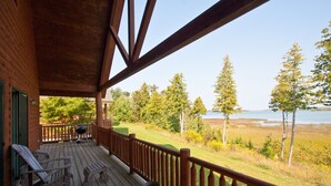A wooden deck with a railing, outdoor seating, and a view of a lake and forest. - Drummond Island Resort (Drummond Island)