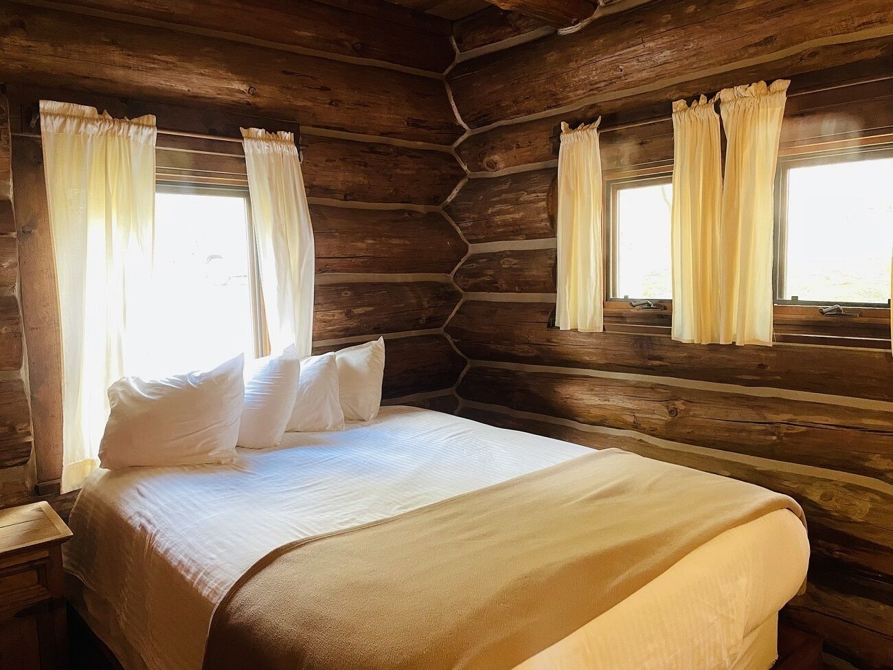 A log cabin-style bedroom with a bed, curtains, and wooden walls.
