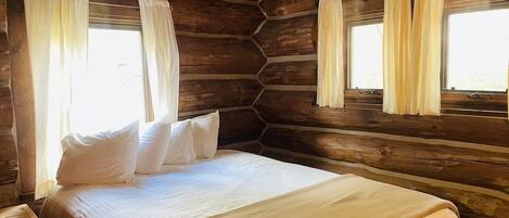 A log cabin-style bedroom with a bed, curtains, and wooden walls.