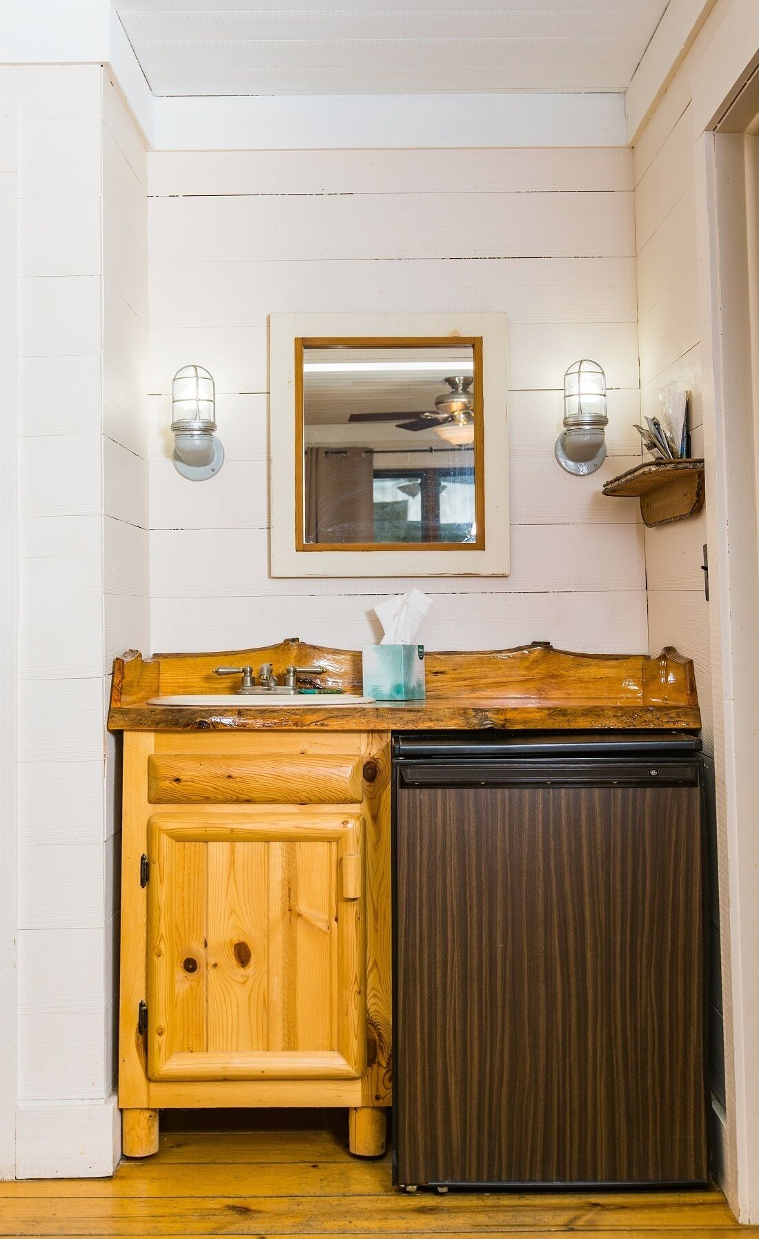 A wooden cabinet with a sink, a mirror above it, and two wall-mounted light fixtures.