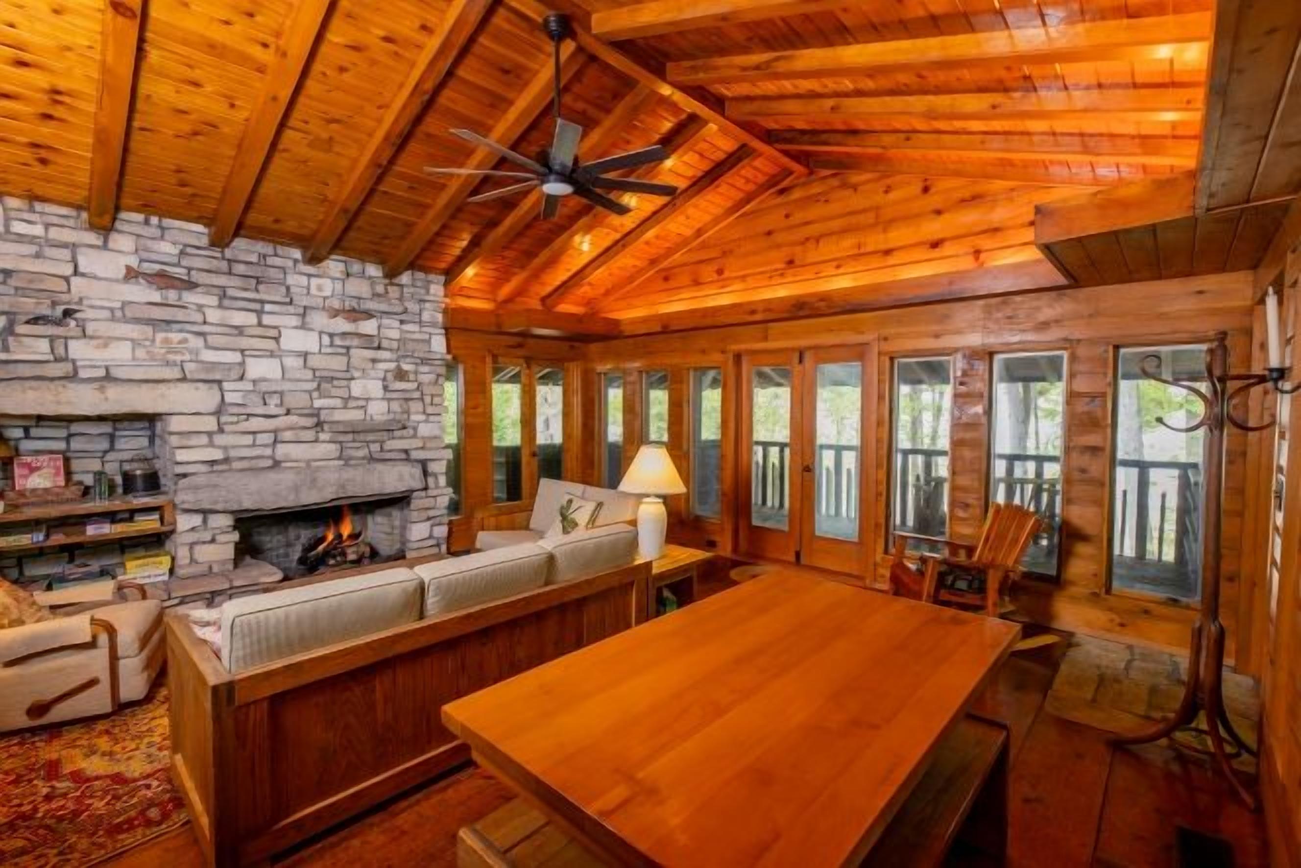 A log cabin interior with a stone fireplace, wooden ceiling, and a dining area.