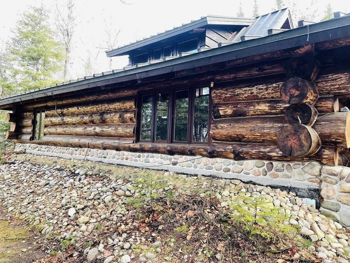 A log cabin with a stone foundation, large windows, and a metal roof.
