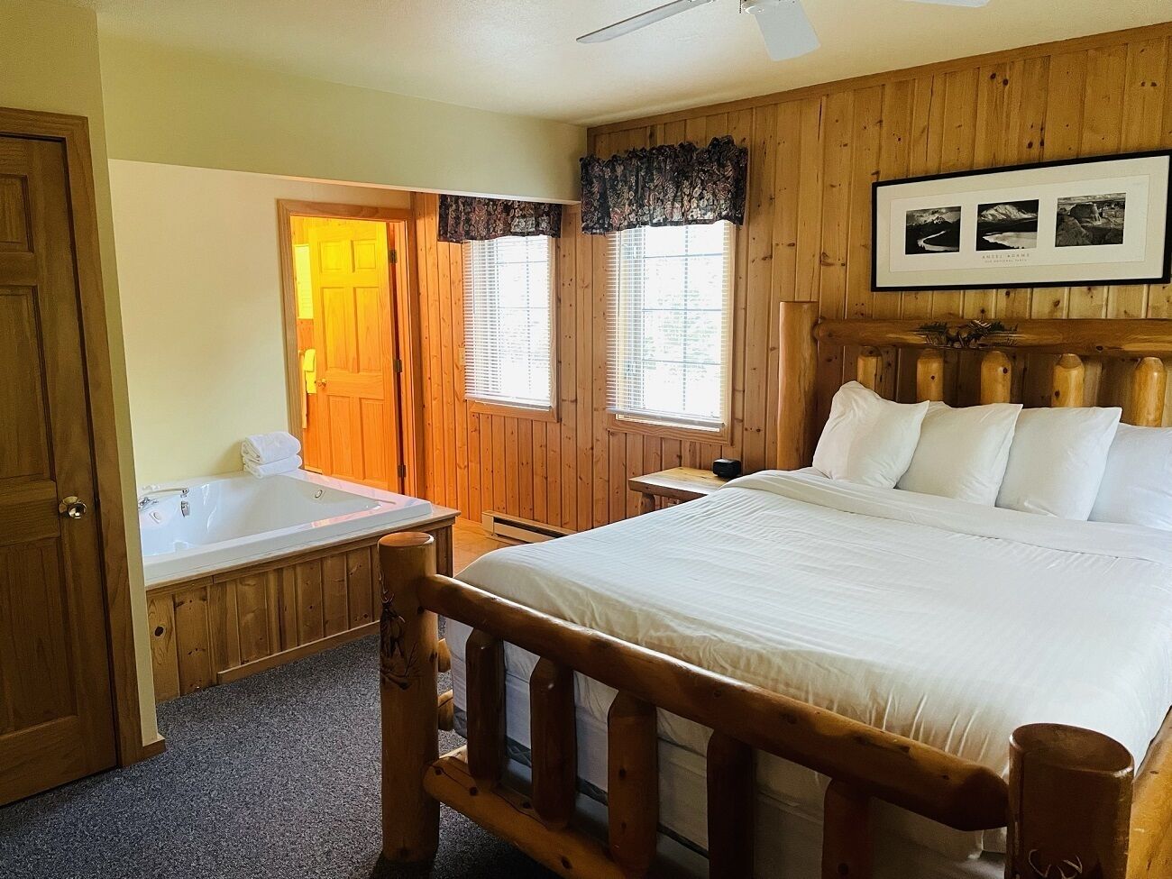 A wooden cabin-style bedroom with a large bed, a wooden bench, a bathtub, and a window with blinds.