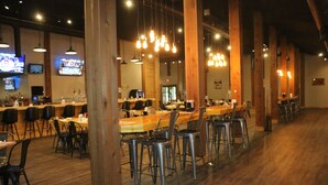 A restaurant with long communal tables, metal chairs, hanging light fixtures, and wooden beams. - Drummond Island Resort (Drummond Island)