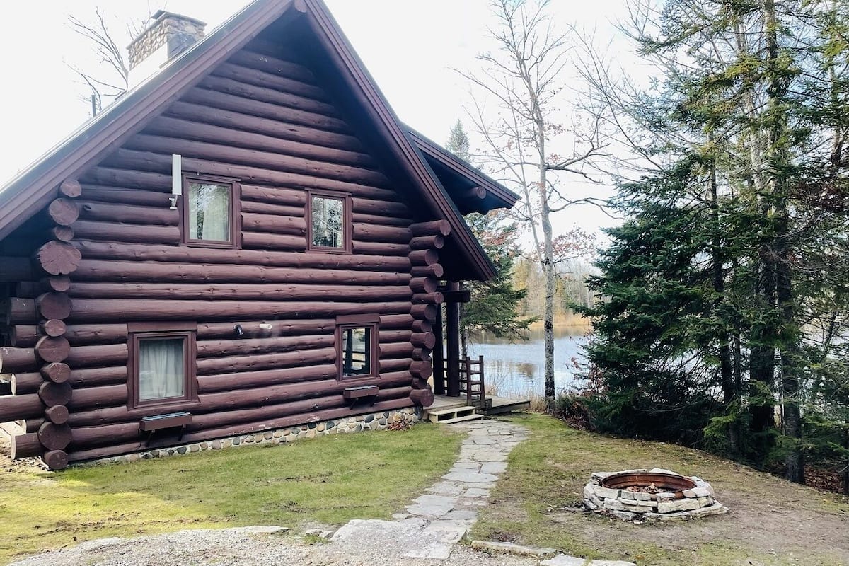 A log cabin with a stone pathway leading to a fire pit.