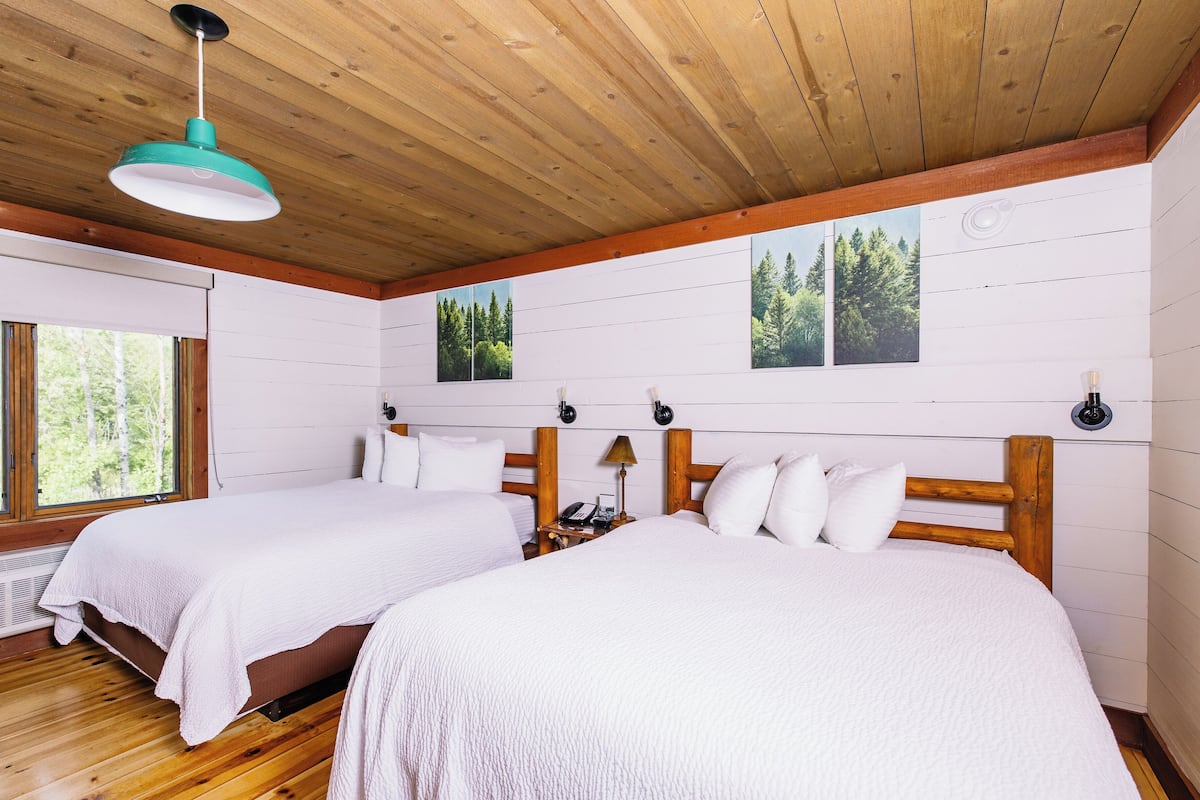 A room with two beds, wooden floors, white walls, and a wooden ceiling.