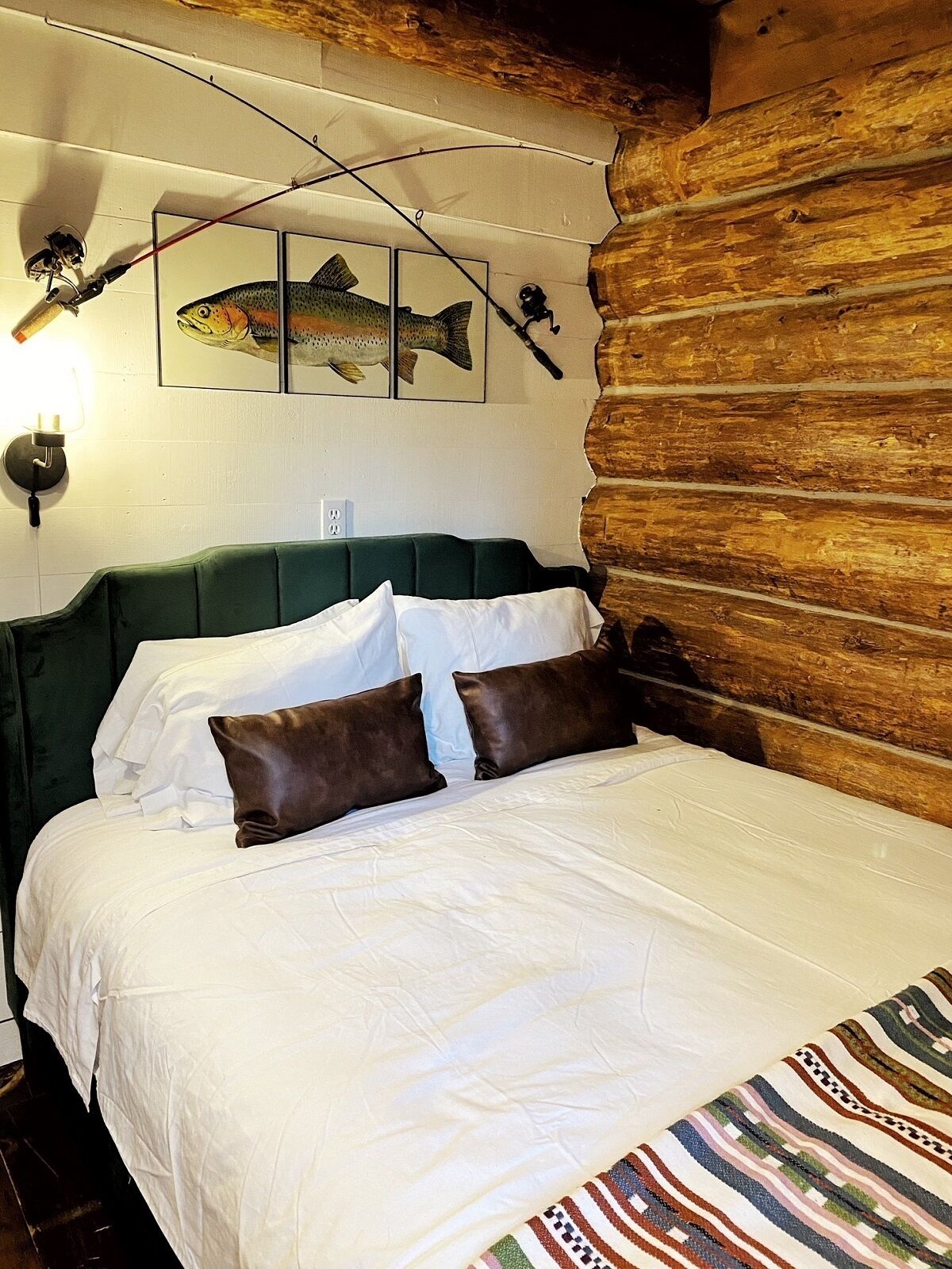A bed with white bedding and brown pillows, a green upholstered headboard, and a wooden log wall.
