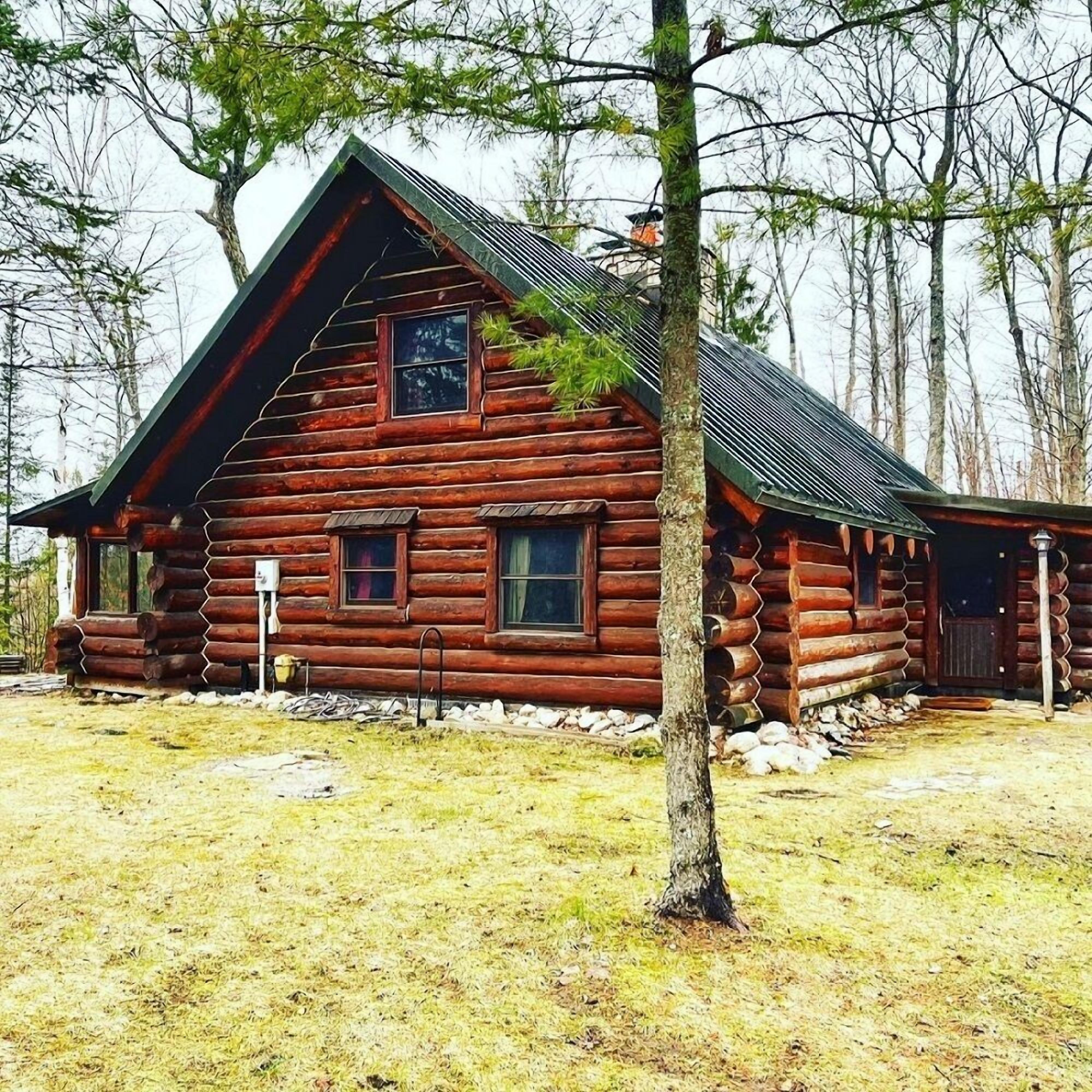 Une cabane en rondins avec un toit à pignon très incliné, un porche à l’avant et des fondations en pierre.
