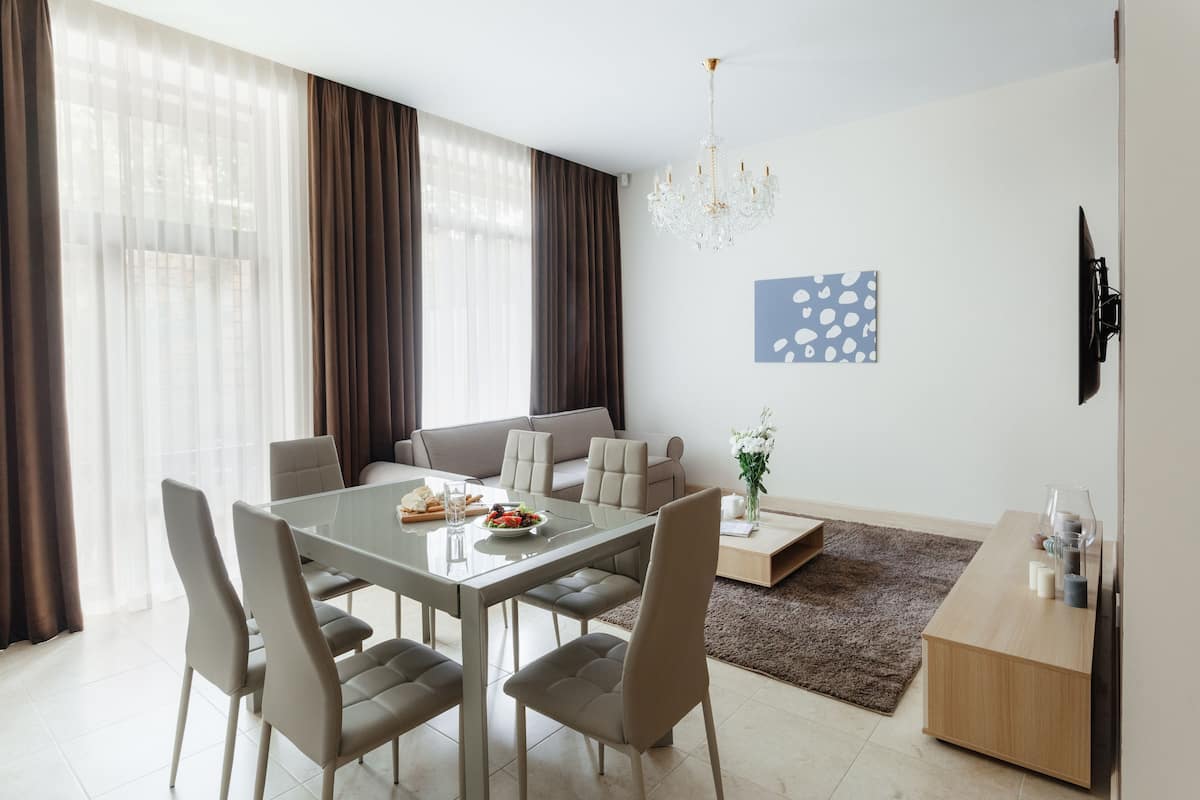 Una sala de estar moderna con una mesa de comedor, sofás, una araña y un televisor de pantalla plana.