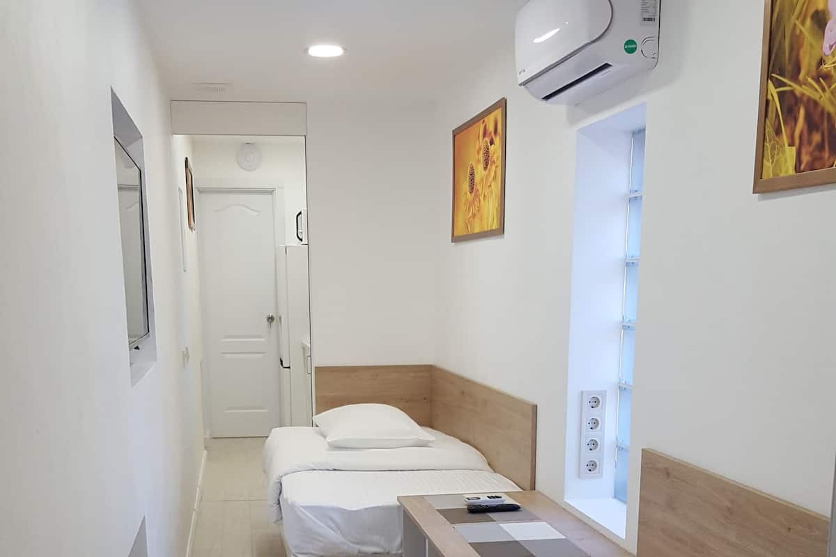 Pasillo que conduce a una habitación con tres camas, un equipo de aire acondicionado y una ventana con persianas.