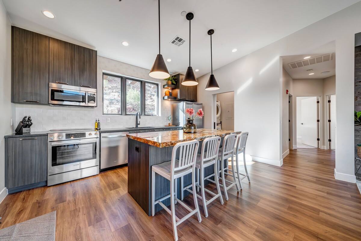A modern kitchen with dark wood cabinets, stainless steel appliances, a large island with bar stools, and pendant lighting.