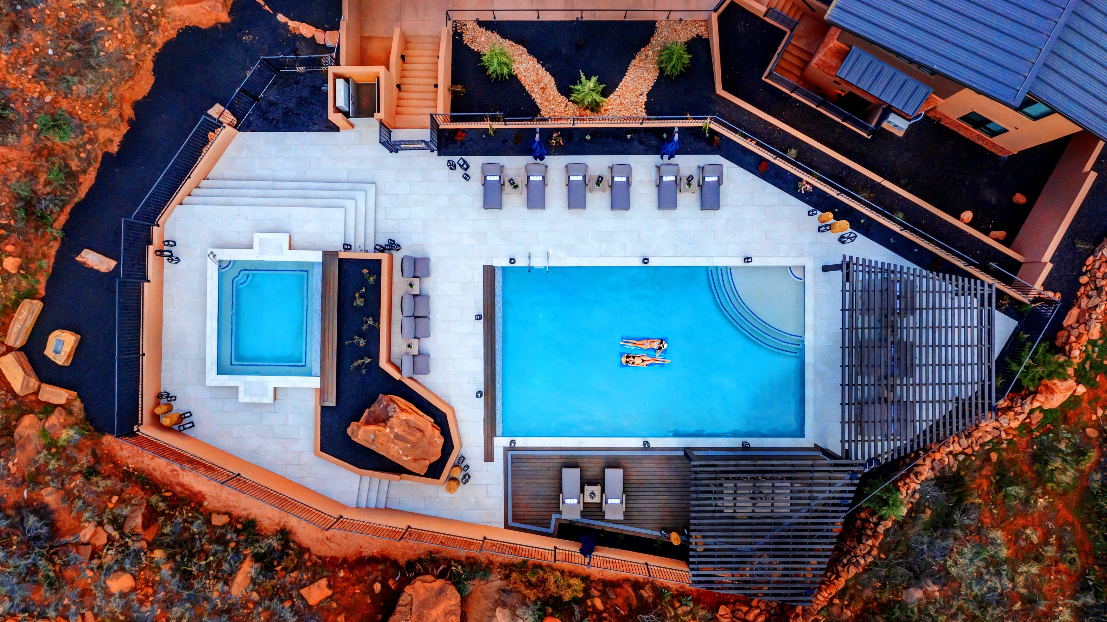 An aerial view of a resort with a large central pool, a smaller adjacent pool, and a separate spa area with a hot tub.