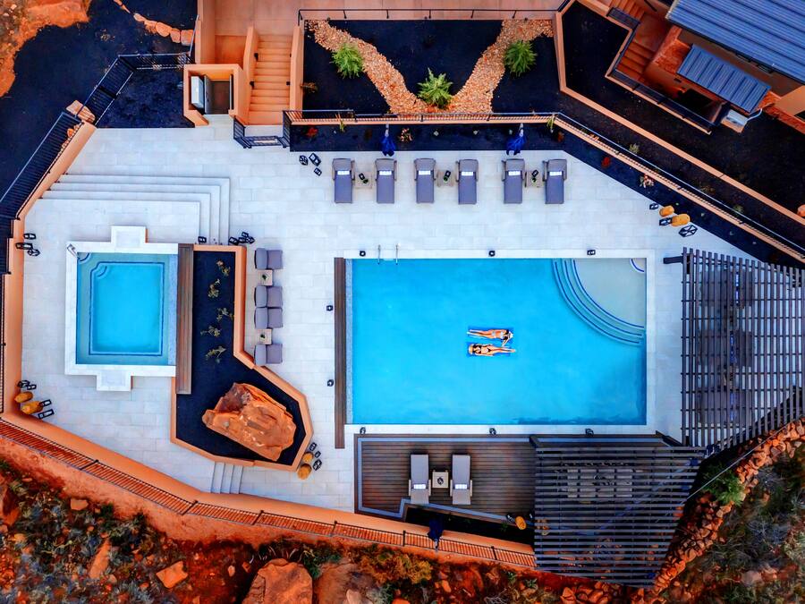 An aerial view of a resort with a large central pool, a smaller adjacent pool, and a separate spa area with a hot tub.