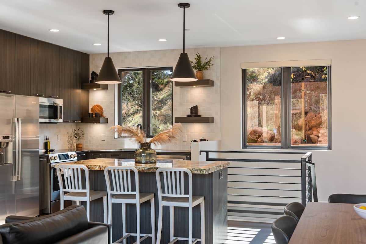 A modern kitchen with a central island, bar stools, and pendant lighting.