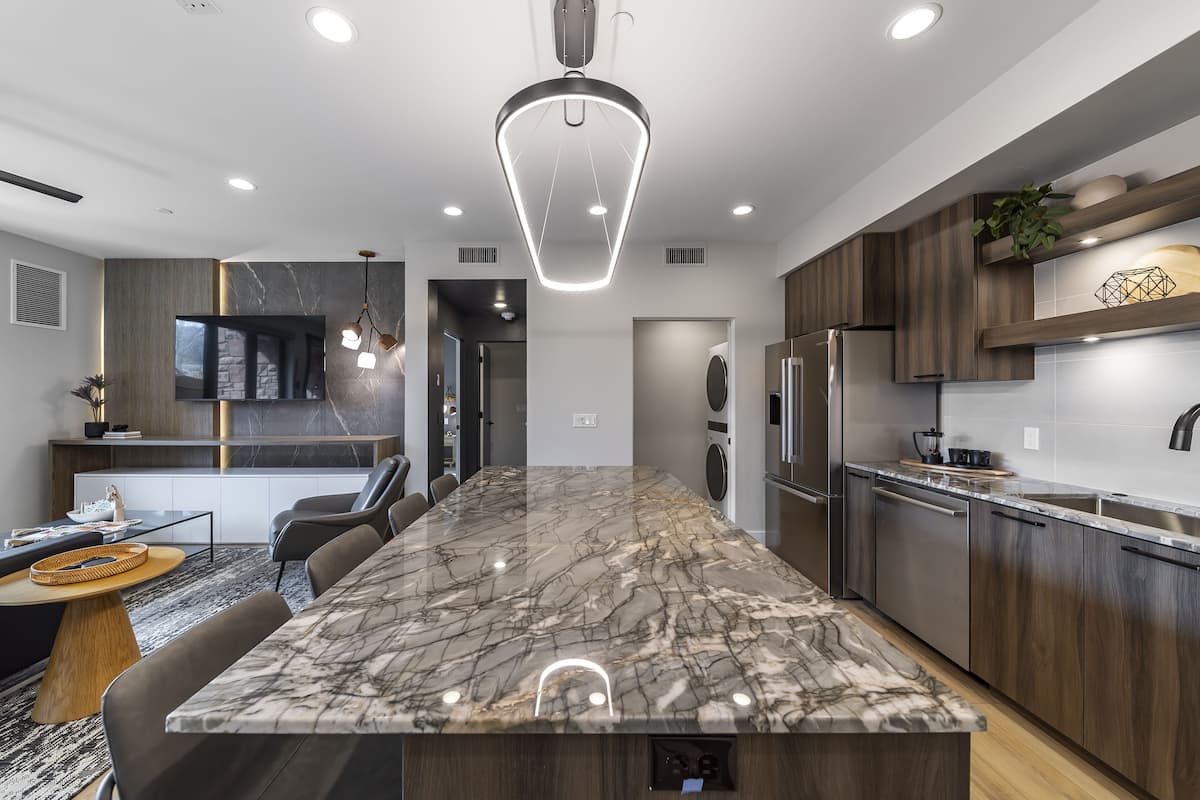 A modern kitchen with a large marble island, wooden cabinets, and built-in appliances.