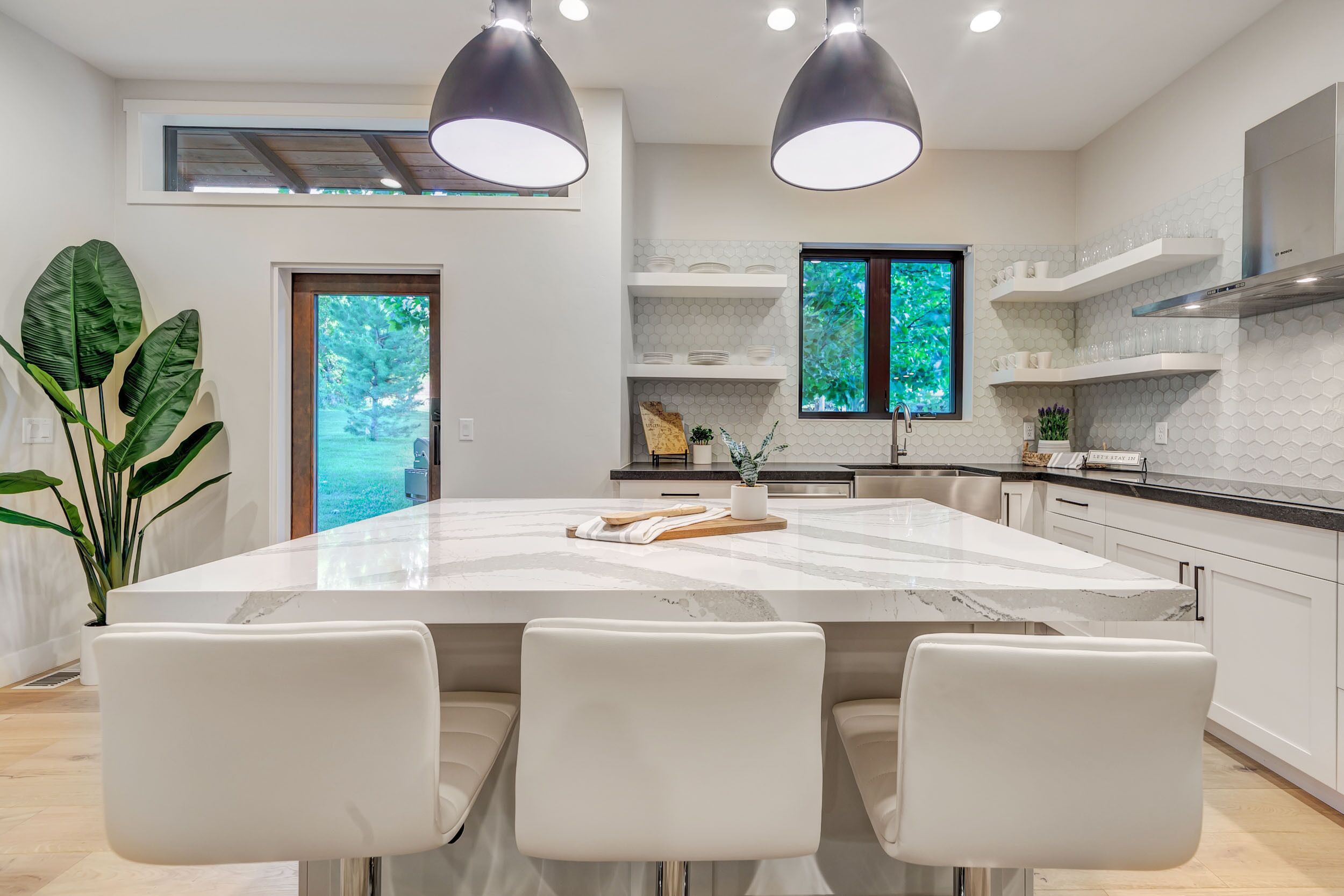 A modern kitchen with a large island, white cabinetry, and pendant lighting.