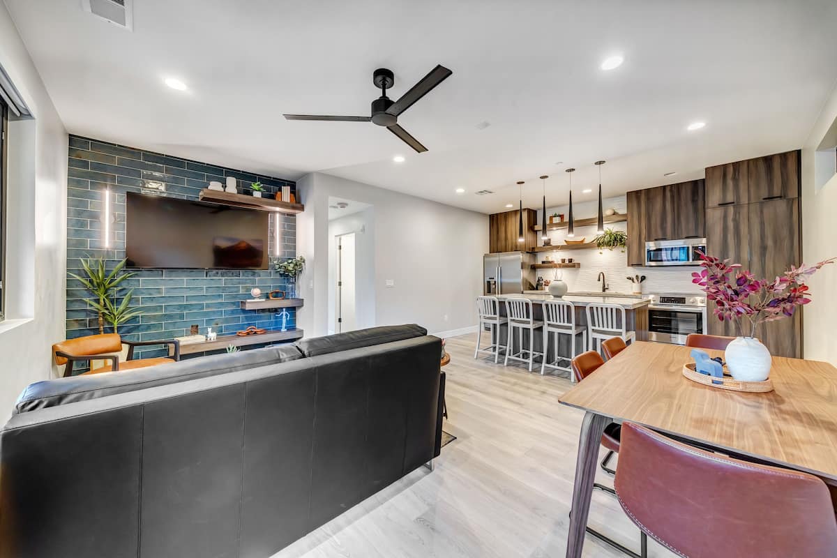 A modern kitchen with a central island, a dining area with a wooden table, and a black leather sofa.