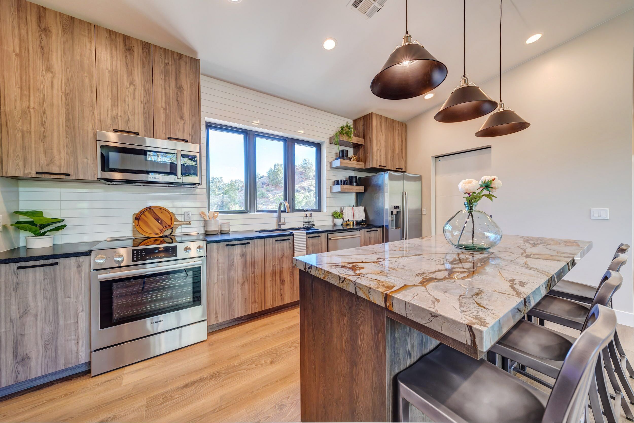 Una cocina moderna con armarios de madera, electrodomésticos de acero inoxidable, una isla de mármol e iluminación colgante.